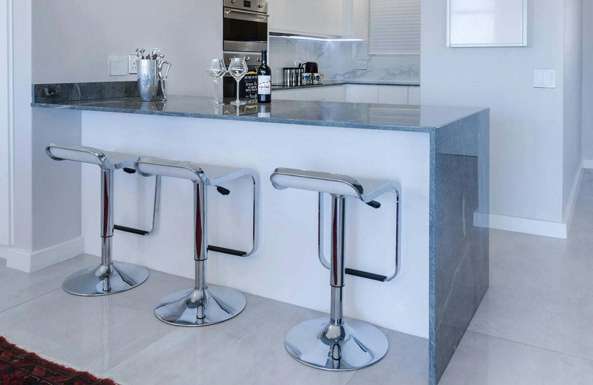 Adjustable bar stools lined along a sleek kitchen island, showing how height-flexible seating works with a modern white and gray kitchen design.