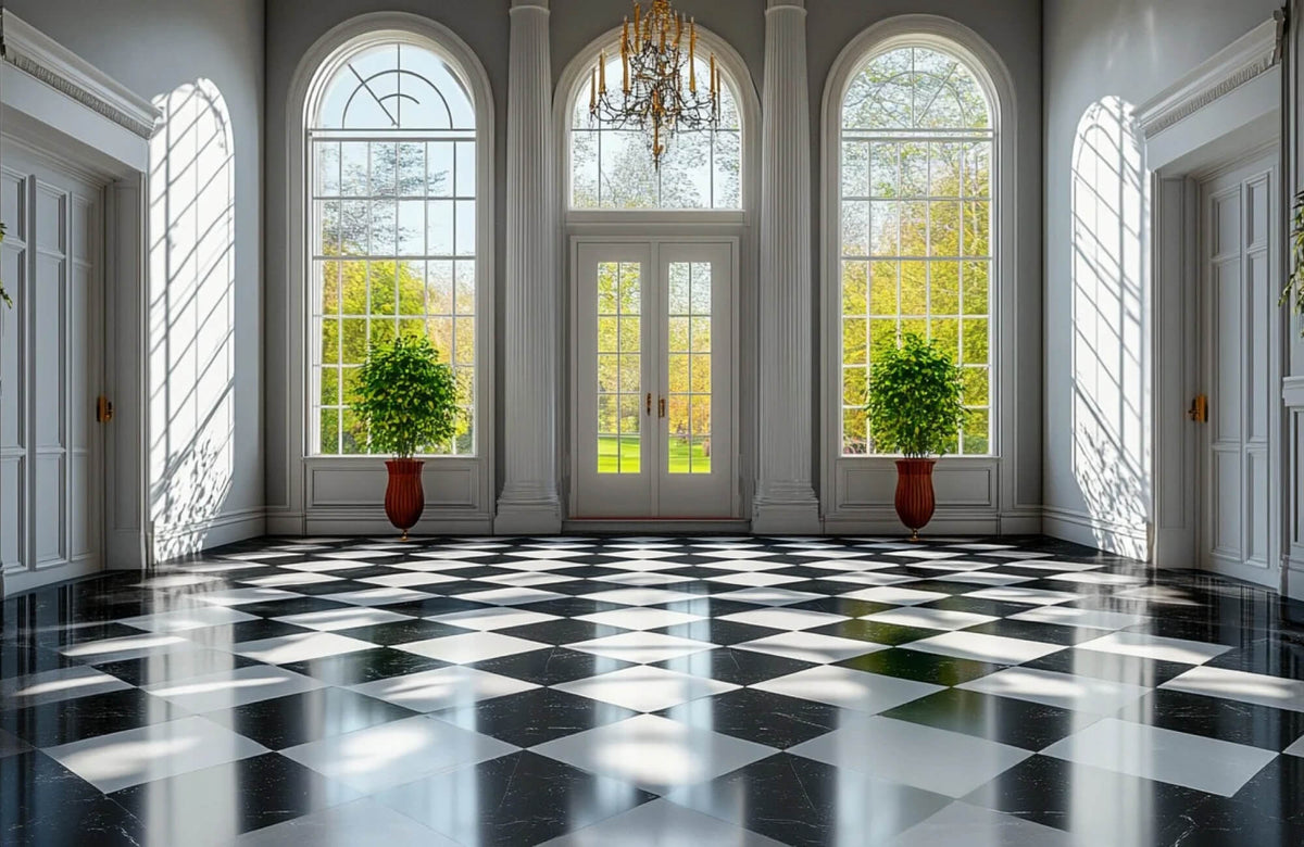 Grand entry hall featuring a polished black and white checkerboard marble floor, framed by tall arched windows, white columns, and a classic chandelier.