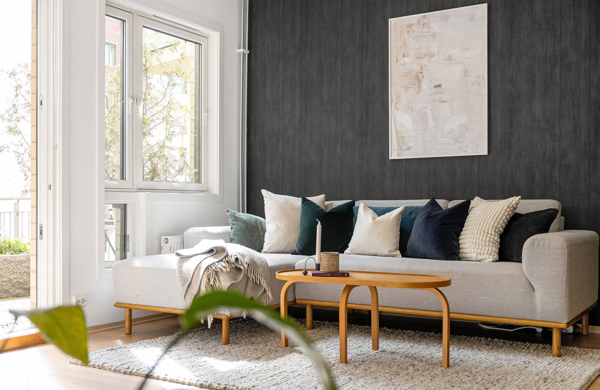 Decorative pillow arrangement on a light gray sectional sofa, featuring cream, deep green, and navy cushions styled against a dark accent wall in a modern living room.