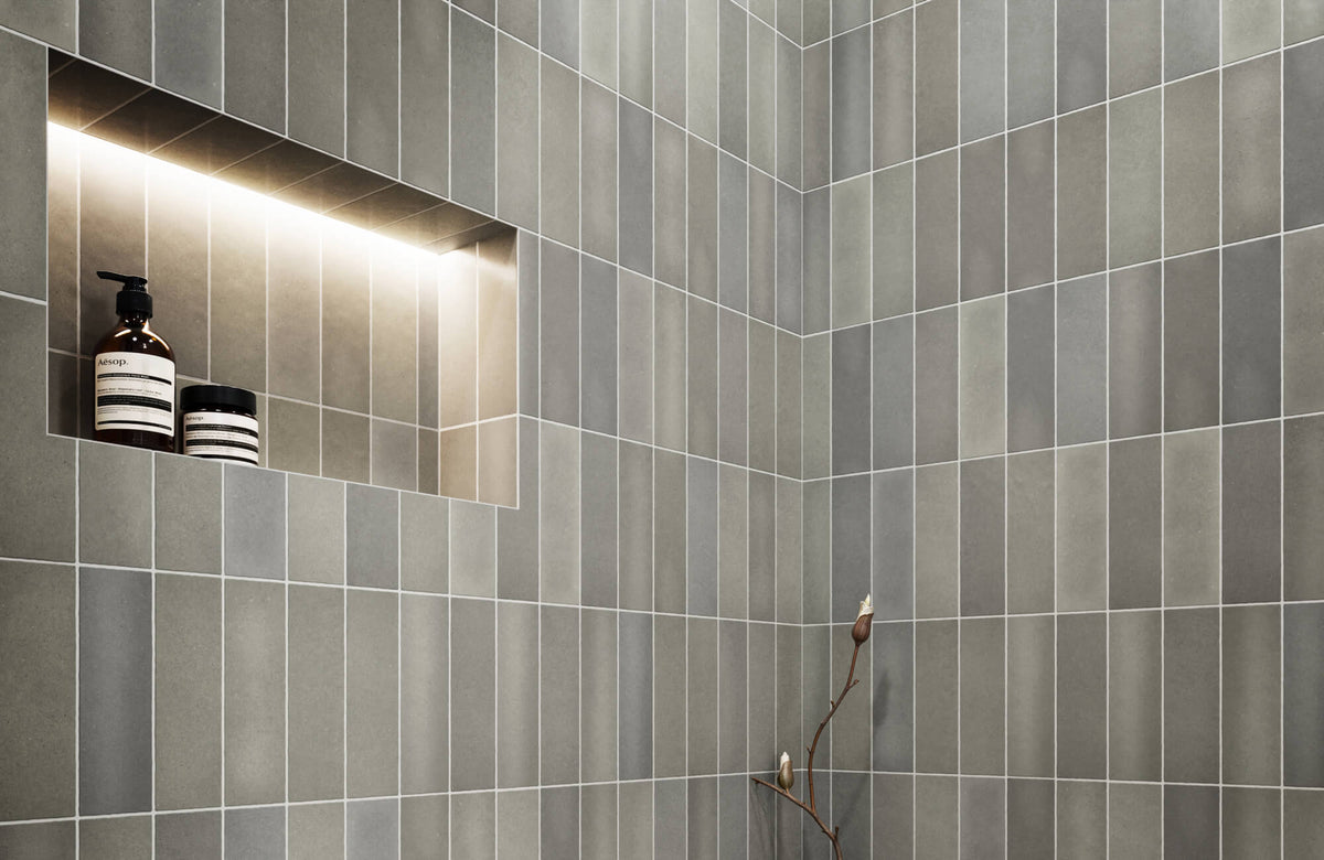 Modern shower featuring matte subway tiles in soft gray tones, highlighted by a recessed shelf with warm lighting for a sleek, functional design.