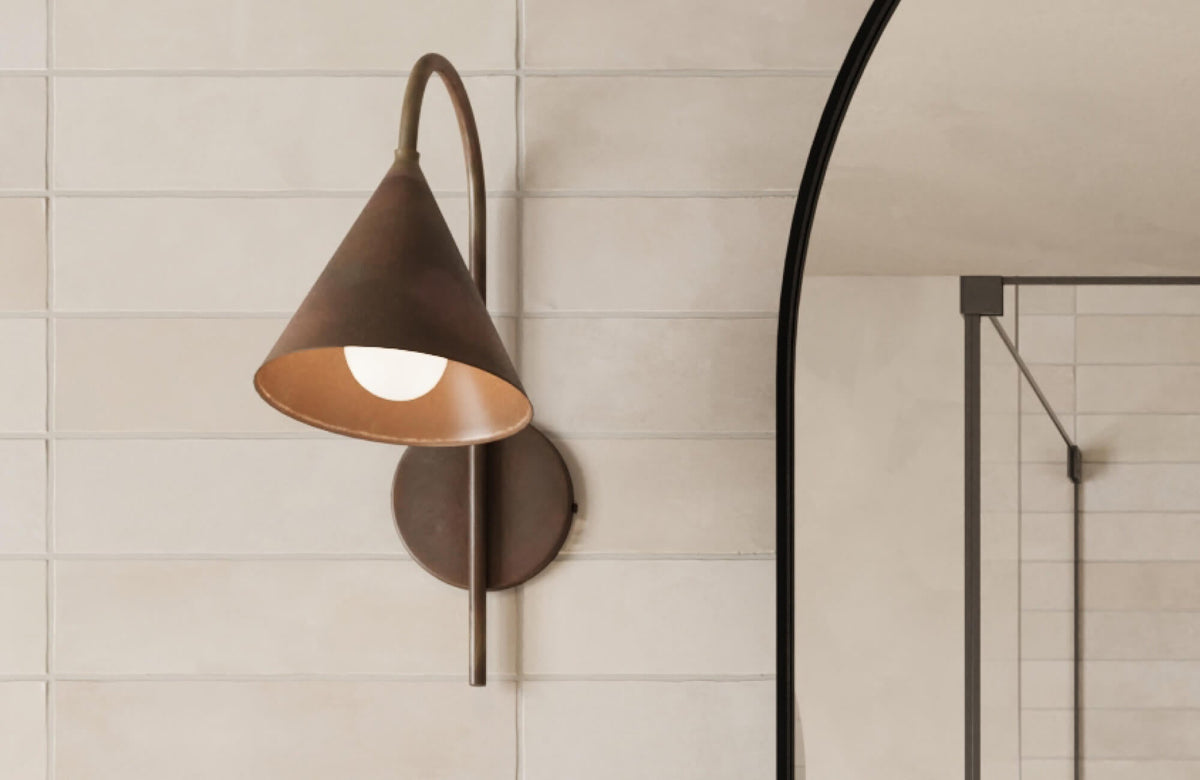 Creamy matte rectangular tiles with subtle texture form a sleek backdrop behind a modern bronze wall sconce.