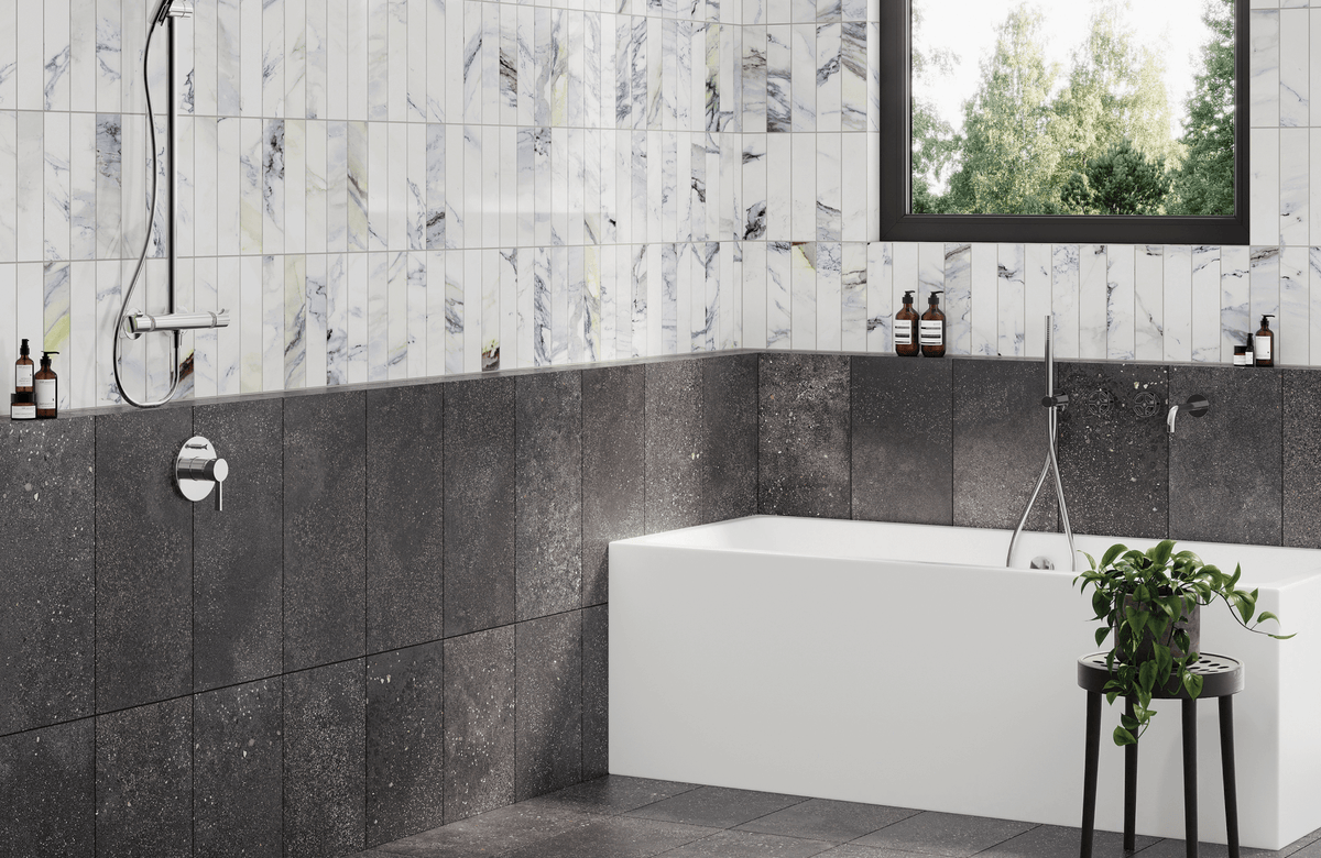 Modern bathroom with polished white marble-look vertical tiles, dark charcoal stone-look wall and floor tiles, a rectangular white tub, chrome shower fixtures, and a black-framed window overlooking greenery.