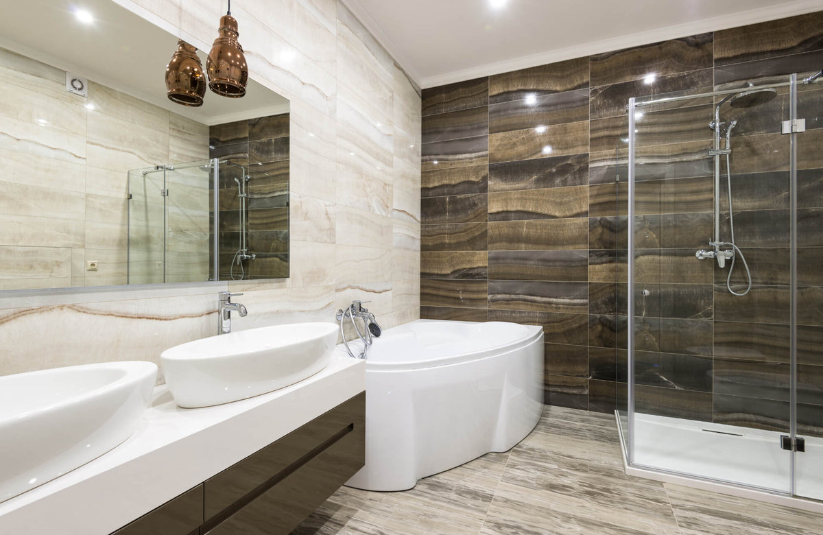 Modern bathroom featuring glossy brown and beige ceramic wall tiles, a glass shower enclosure, dual sinks, and a corner bathtub.