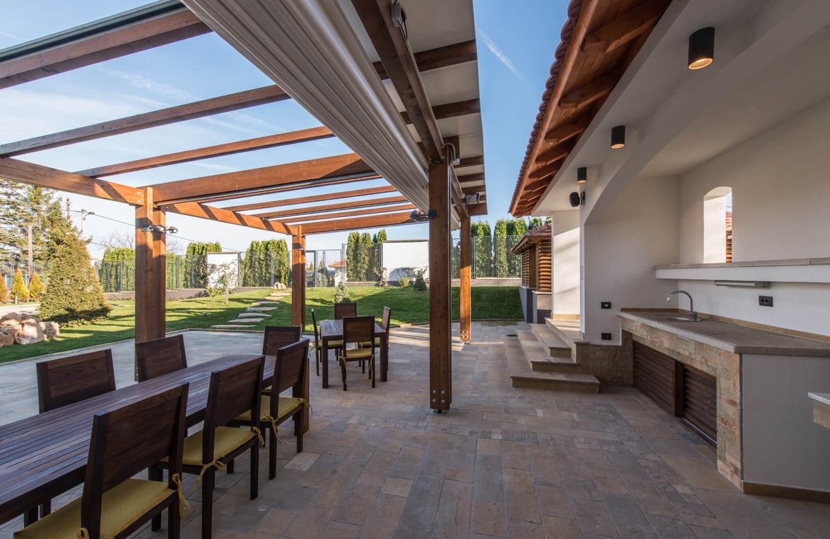 Modern outdoor dining patio with dark porcelain tiles under a wood pergola, showing durable flooring performance in direct sunlight.