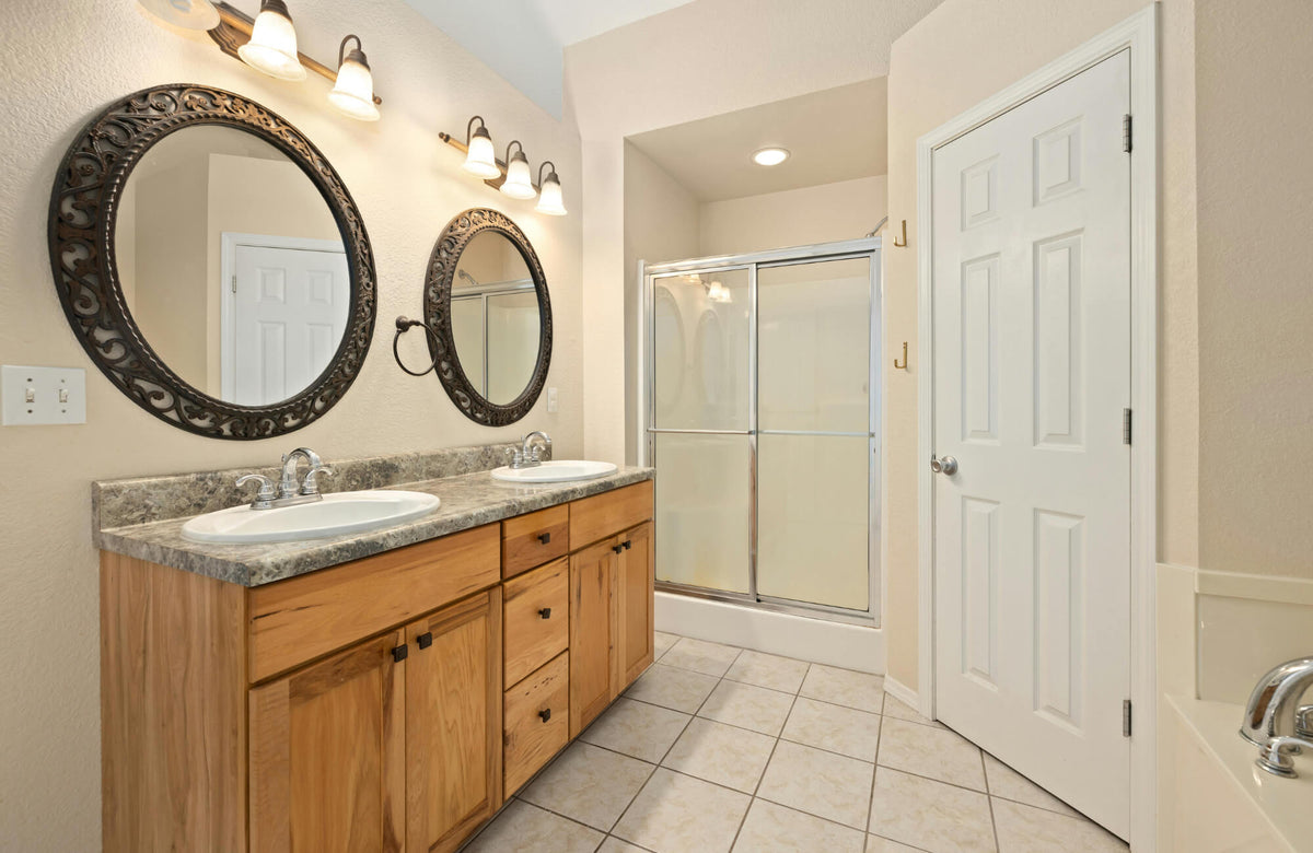 Guest bathroom featuring a 60 inch double sink vanity with wood cabinetry, round mirrors, and ample walkway space for comfortable circulation.