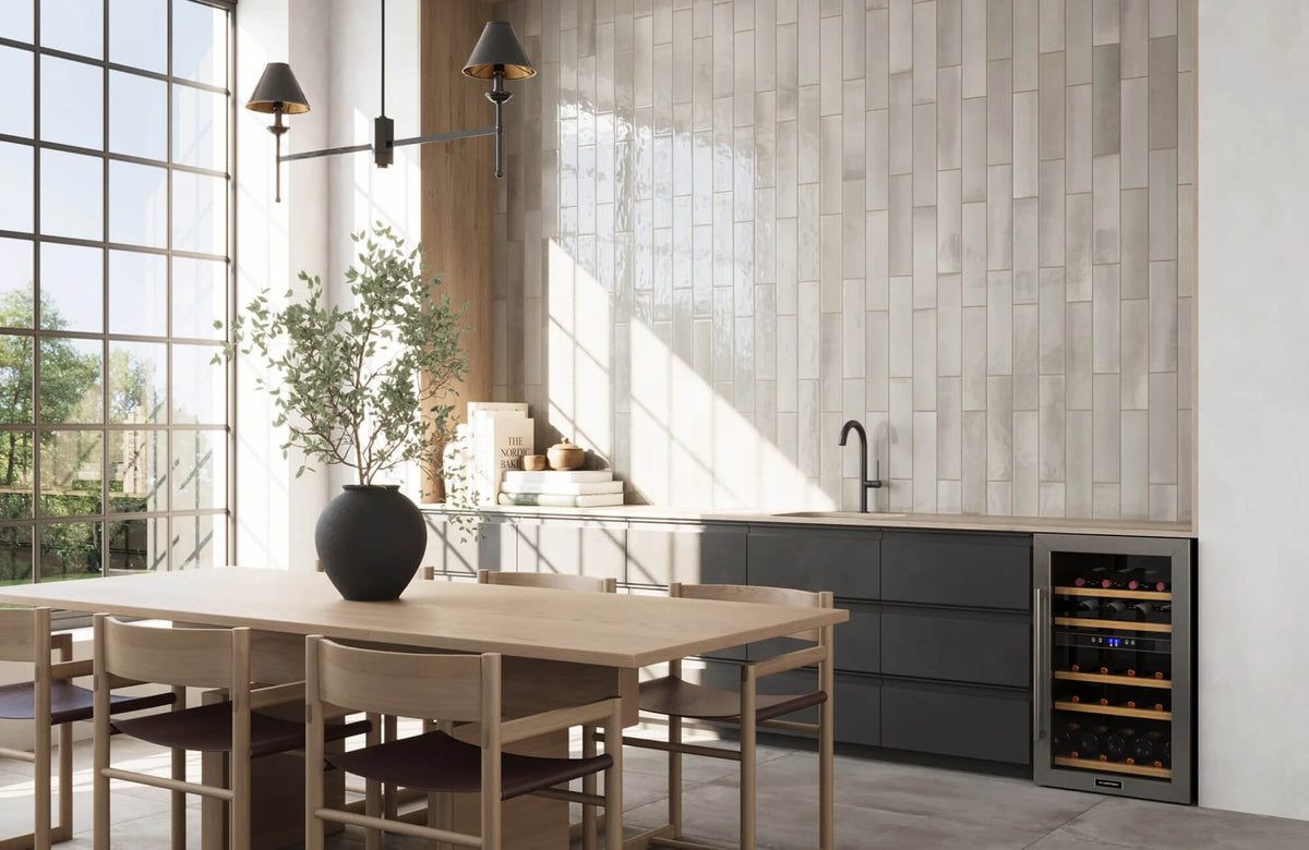Modern kitchen featuring a sleek black faucet, wine cooler, and vertically offset large format beige subway tile backsplash, with natural light streaming in through large windows.