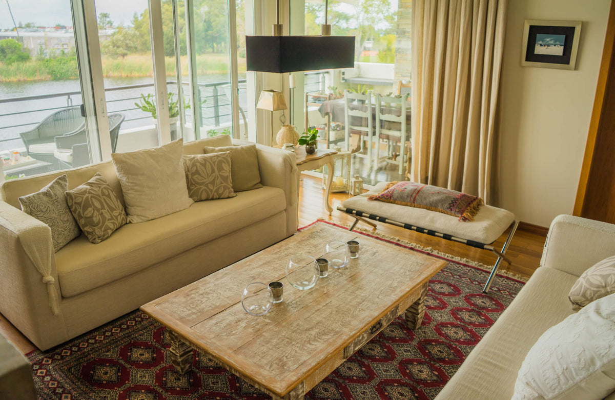 Cozy living room with beige sofas, rustic wood coffee table, and red patterned rug overlooking a river view.
