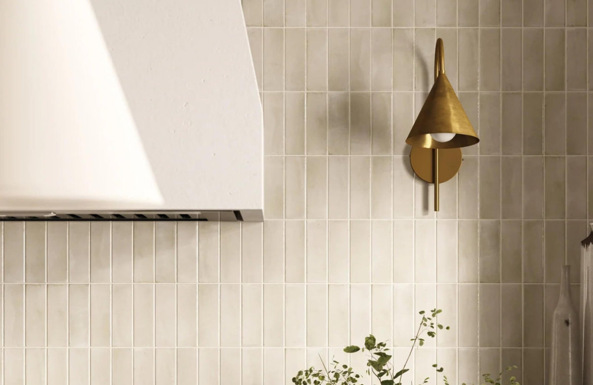 Modern kitchen backsplash featuring vertically stacked cream subway tiles, a white range hood, and a brass wall sconce that creates a warm and refined atmosphere.