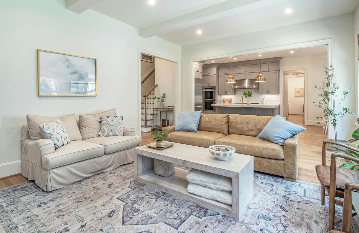 Neutral living room with beige and tan sofas styled with textured pillows and layered rug in open concept space.