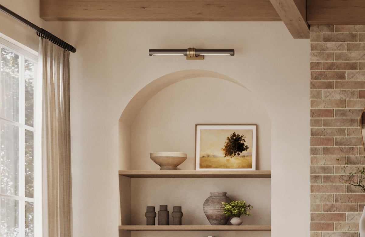 Cozy arched wall niche with a brass picture light, open shelving, neutral pottery, framed landscape art, and warm brick accent wall.