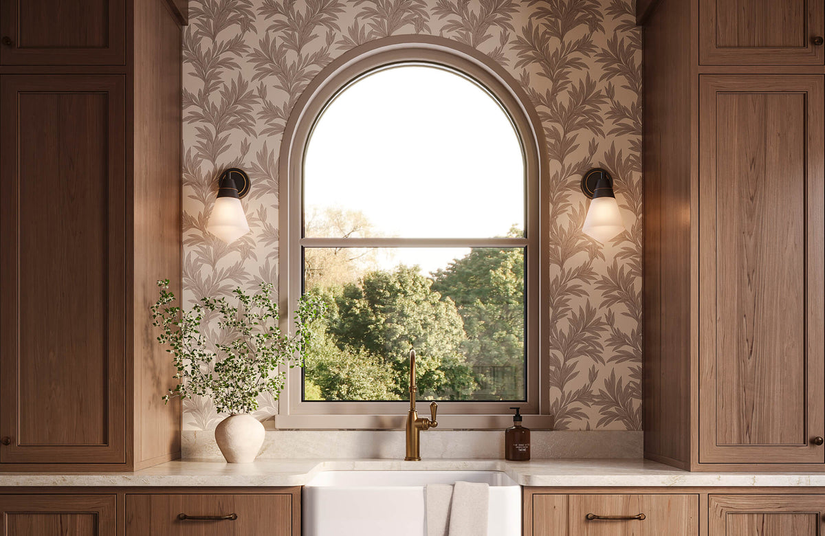 Warm kitchen interior featuring botanical wallpaper around an arched window, complemented by natural wood cabinetry, brass fixtures, and soft daylight that enhances the layered neutral palette.
