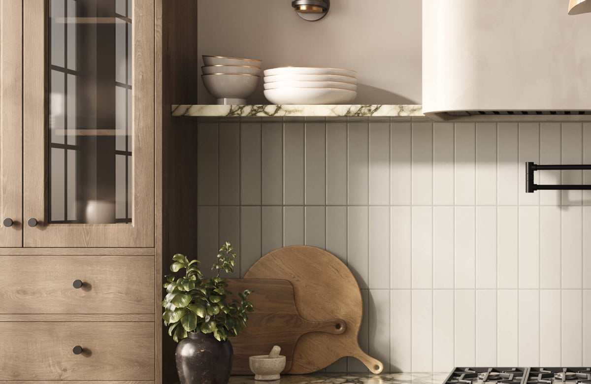 Vertical stacked subway tile pantry backsplash in a soft beige tone, paired with wood cabinetry, a marble shelf, and neutral kitchen decor, including cutting boards and a potted plant.