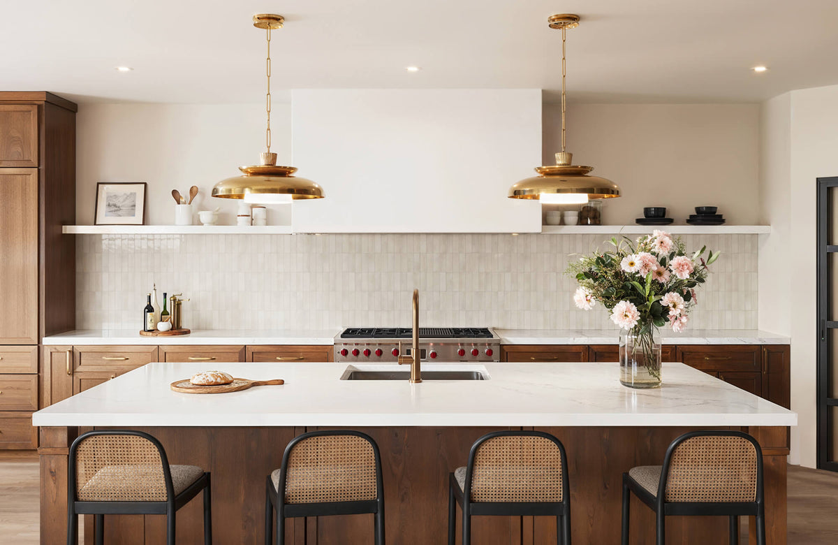 Cream subway tile backsplash in a modern kitchen with white countertops, warm wood cabinetry, brass pendant lights, and woven bar stools.