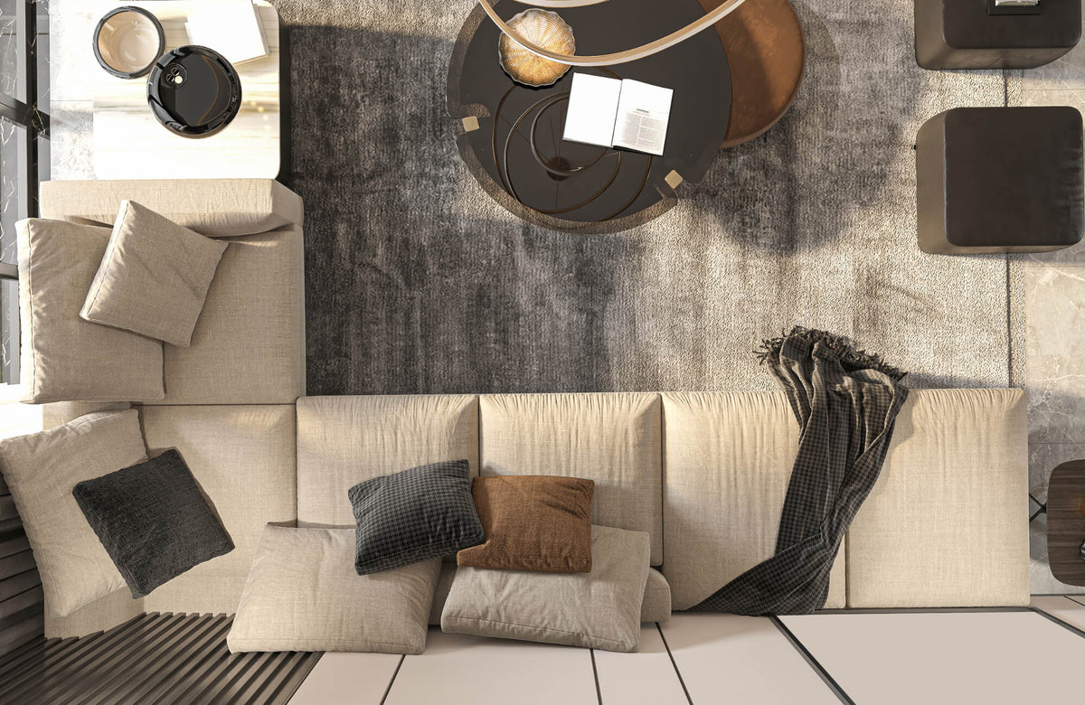 Top view of a modern living room with a neutral sofa styled with solid and patterned down pillows, layered over a textured area rug.