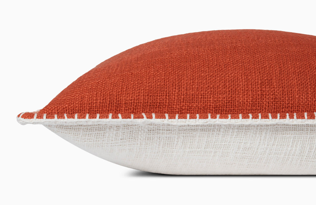 Rust textured decorative pillow with white whipstitch trim and neutral linen backing on a light gray background.