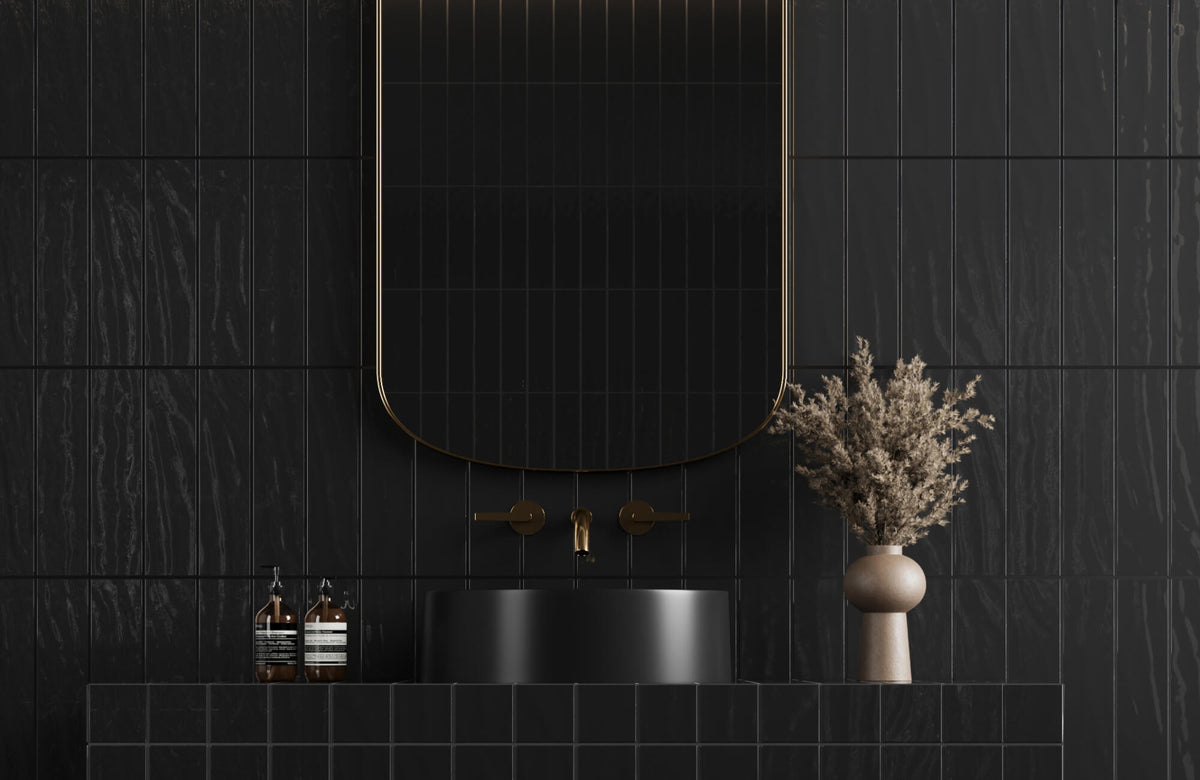 Modern black bathroom with textured subway tile wall, a curved mirror with gold trim, a matte black sink, and brass fixtures.