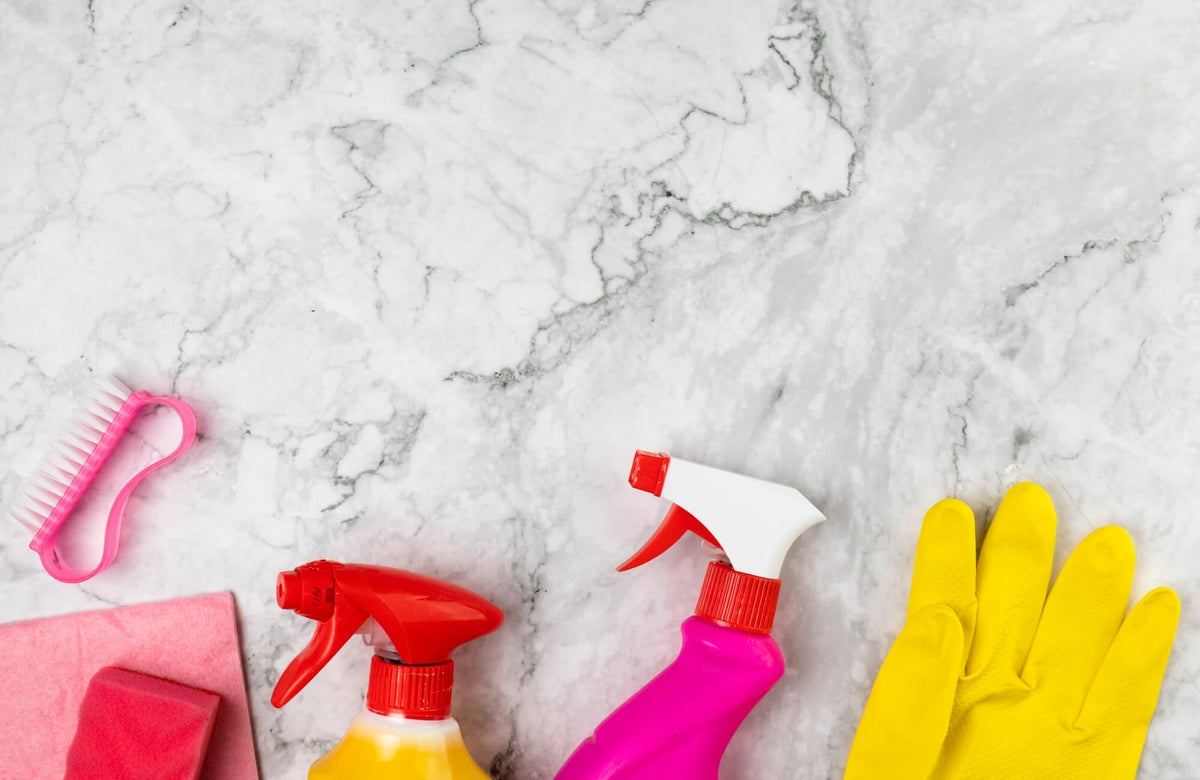 Cleaning supplies arranged on a white marble surface with subtle gray veining and smooth polished finish.