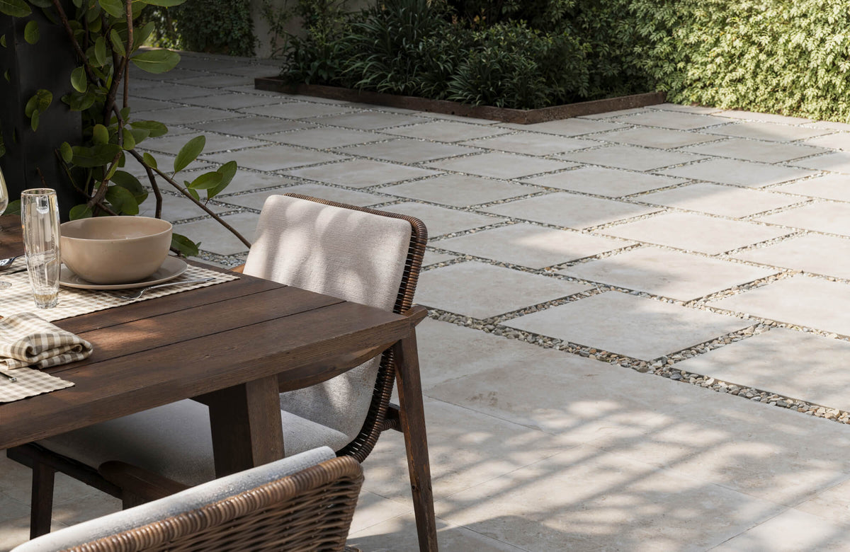 Outdoor dining area featuring neutral porcelain pavers set with stones, surrounded by greenery for a natural, relaxed look.