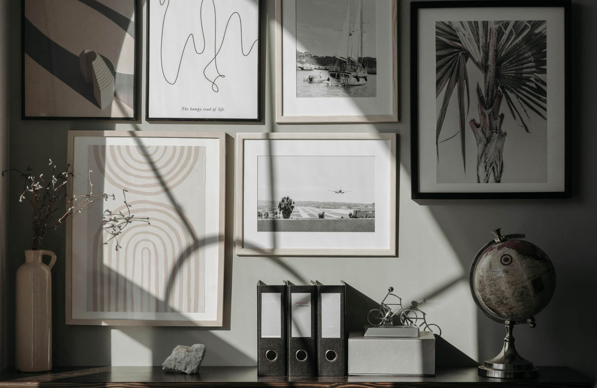Layered gallery wall featuring minimalist framed prints and photographs, softly lit by natural light in a calm, collected interior.