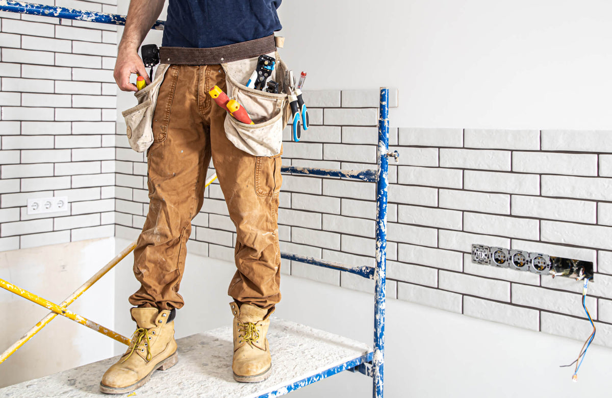 An installer standing on scaffolding while setting white subway tile in a clean horizontal layout, showing how spacing and alignment are established before finishing a tiled wall.