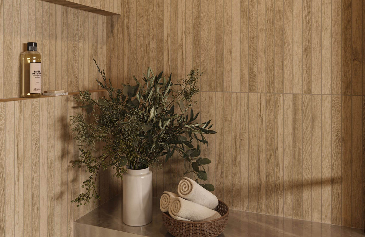 Wood-look porcelain tile wall in warm natural tones with built-in niche, decorative vase with greenery, and rolled towels creating a spa-inspired bathroom setting.