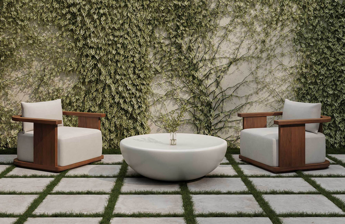 Contemporary outdoor patio seating area with two wood-framed lounge chairs and a sculptural white coffee table set against a lush vine-covered garden wall.
