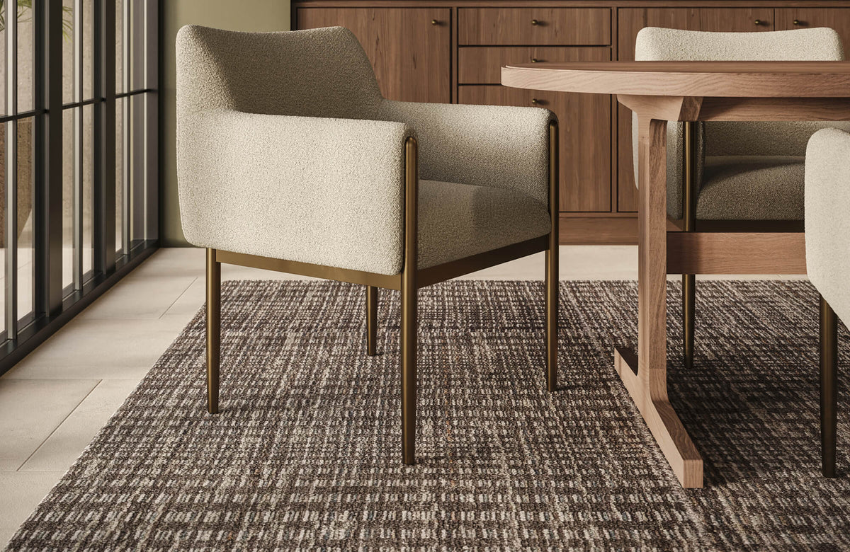 A woven wool rug with tonal brown variation extends beneath the dining table, bringing depth, comfort, and natural texture to the interior.