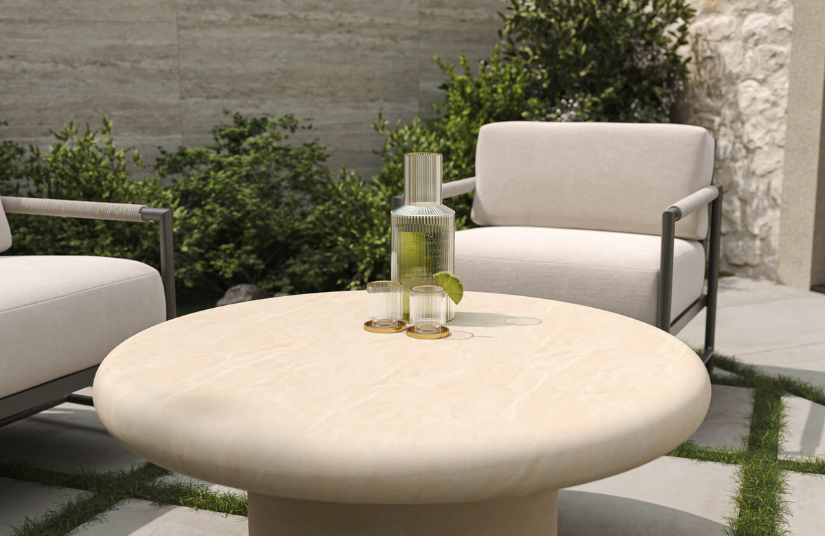 A round beige outdoor coffee table pairs well with lounge chairs, offering a smooth surface for drinks while keeping the layout open and easy to move around.