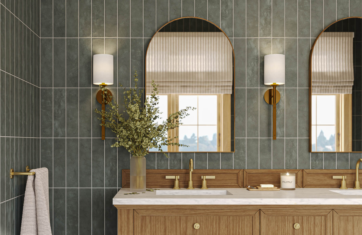 Arch mirror centered above bathroom vanity with brass sconces and green tiled wall backdrop