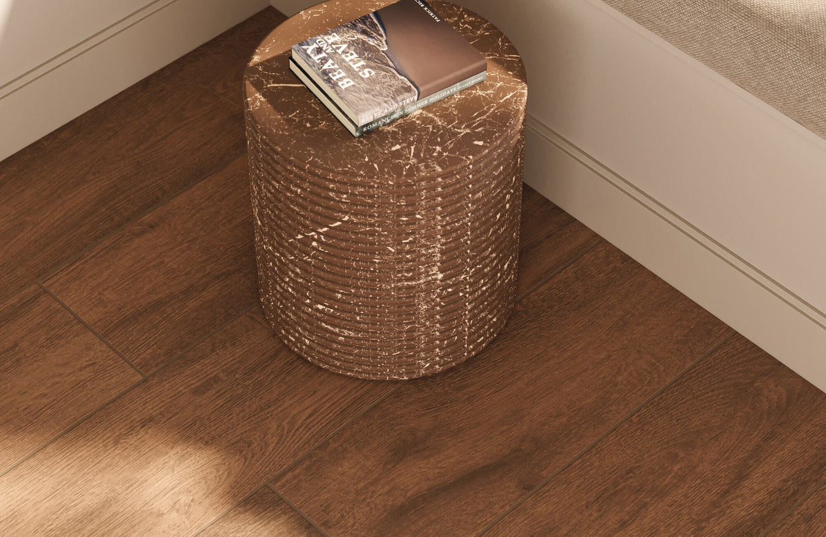 Warm brown wood-look floor tiles featuring realistic wood grain variation, paired with a sculptural side table and minimal living room styling.