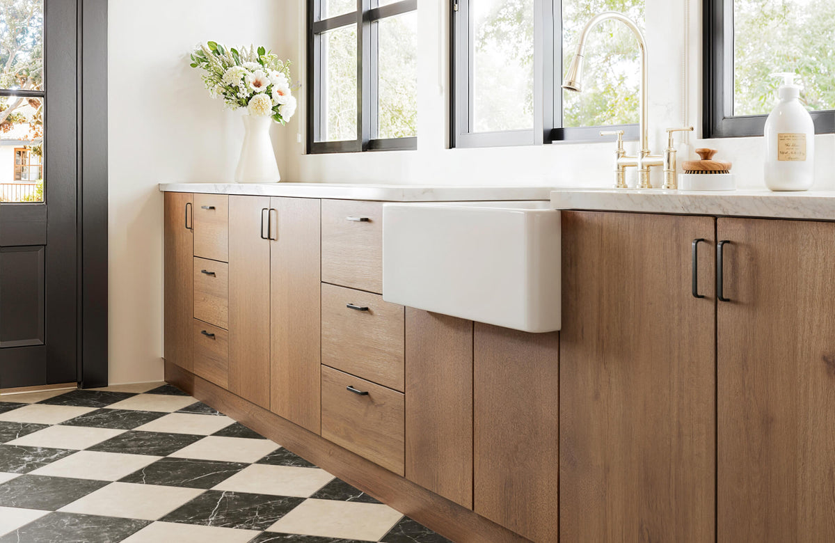 Black and white checkerboard tiles kitchen floor paired with warm wood cabinets, farmhouse sink, and marble countertop.