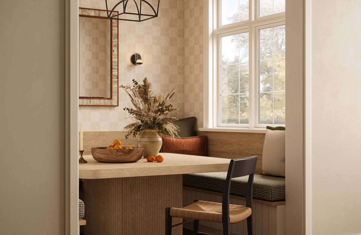 Breakfast nook with textured beige wallpaper, a wood dining table, built-in bench seating, woven chair, black pendant light, wall sconce, and tall windows.