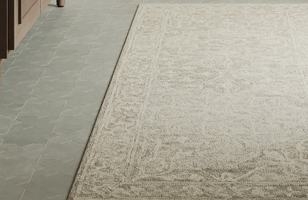 Close-up view of a neutral-toned wool area rug showcasing a soft, textured surface with subtle patterning, placed alongside geometric tile flooring for a refined, modern contrast.