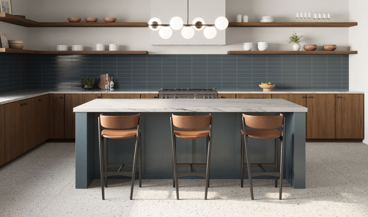 Modern kitchen with deep blue subway tiles, wooden cabinets, and an island with bar stools. Floating shelves hold dishes and decor, and a stylish chandelier illuminates the space