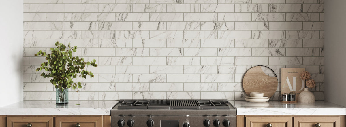 Elegant kitchen backsplash featuring white marble look subway tiles, complemented by light wooden cabinets, a vase of green foliage, and decorative kitchenware