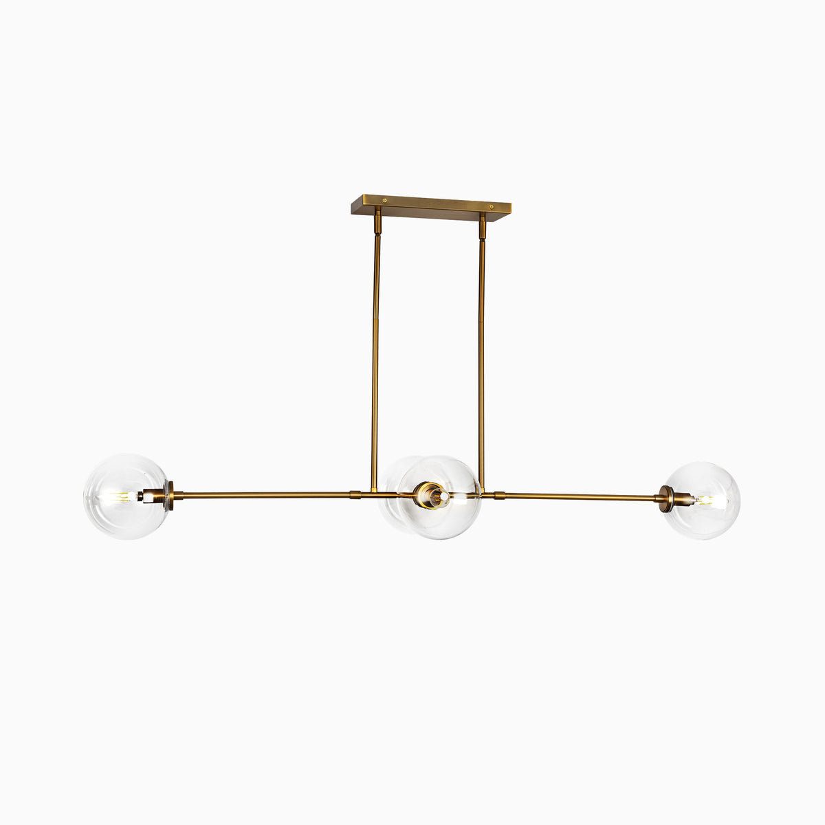 Modern linear pendant light with three clear glass globe shades on a brushed brass horizontal frame.