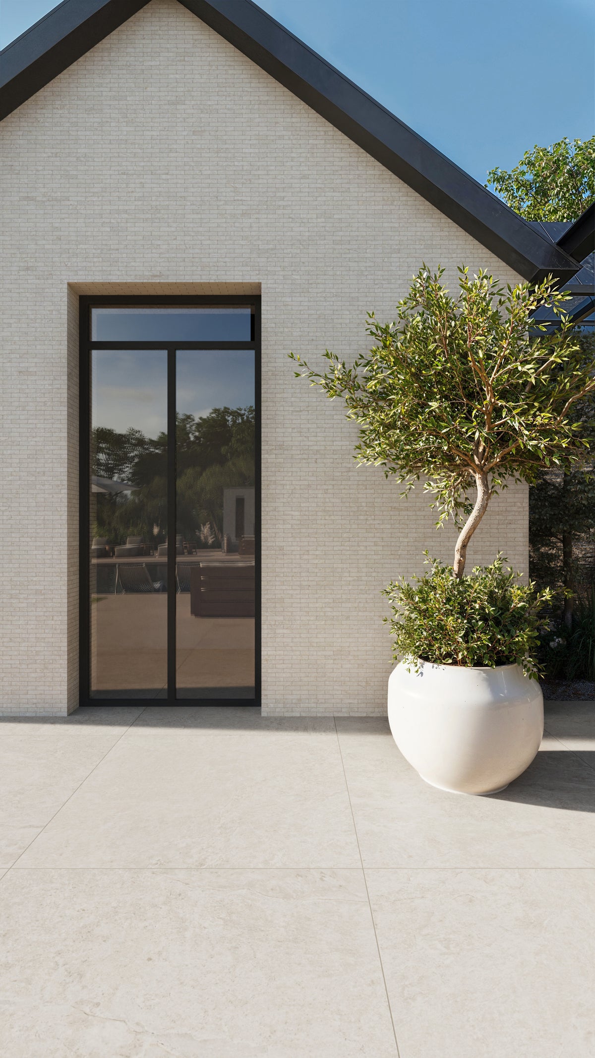 Modern exterior view featuring a light brick wall, large black-framed glass door, and a potted tree on a neutral porcelain tile floor.