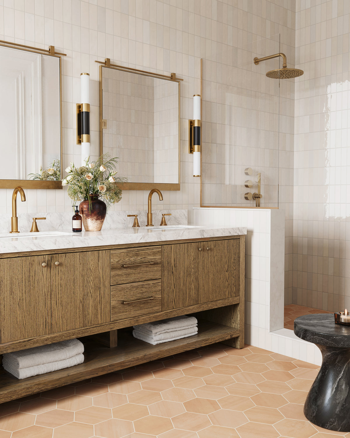Warm bathroom with wood vanity, marble countertop, brass fixtures, and Tomlinson wall sconces flanking mirrors above the sink.