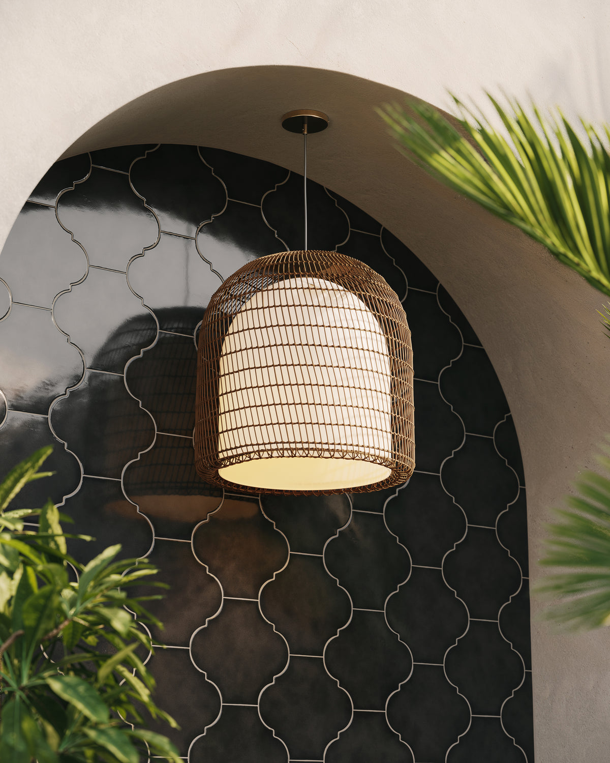 Modern pendant light with handwoven rattan shade and black ceiling canopy in arched tile setting.