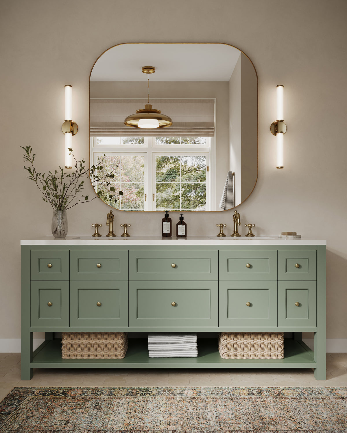 Green double vanity with paneled drawers and brass knobs, topped with a white countertop and dual sinks. A large rounded mirror and vertical brass sconces hang above, while woven baskets and folded towels rest on the open lower shelf beneath the cabinet.