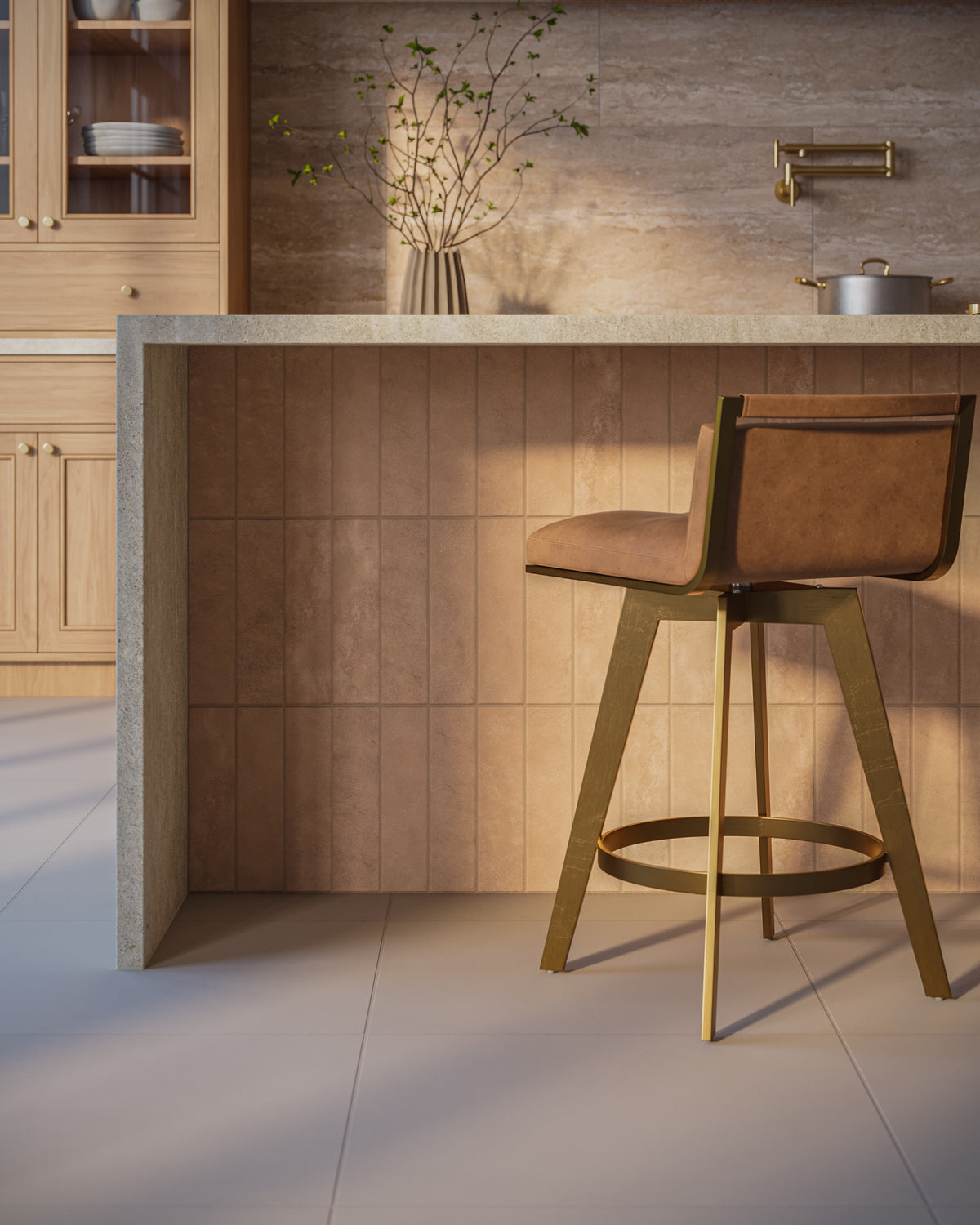Modern kitchen interior featuring a kitchen island clad in rectangular porcelain tiles with a matte finish and lightly textured surface in a warm brown tone, paired with light wood cabinetry, a stone countertop, a brass wall-mounted faucet, and a brown upholstered bar stool on a light neutral tile floor.