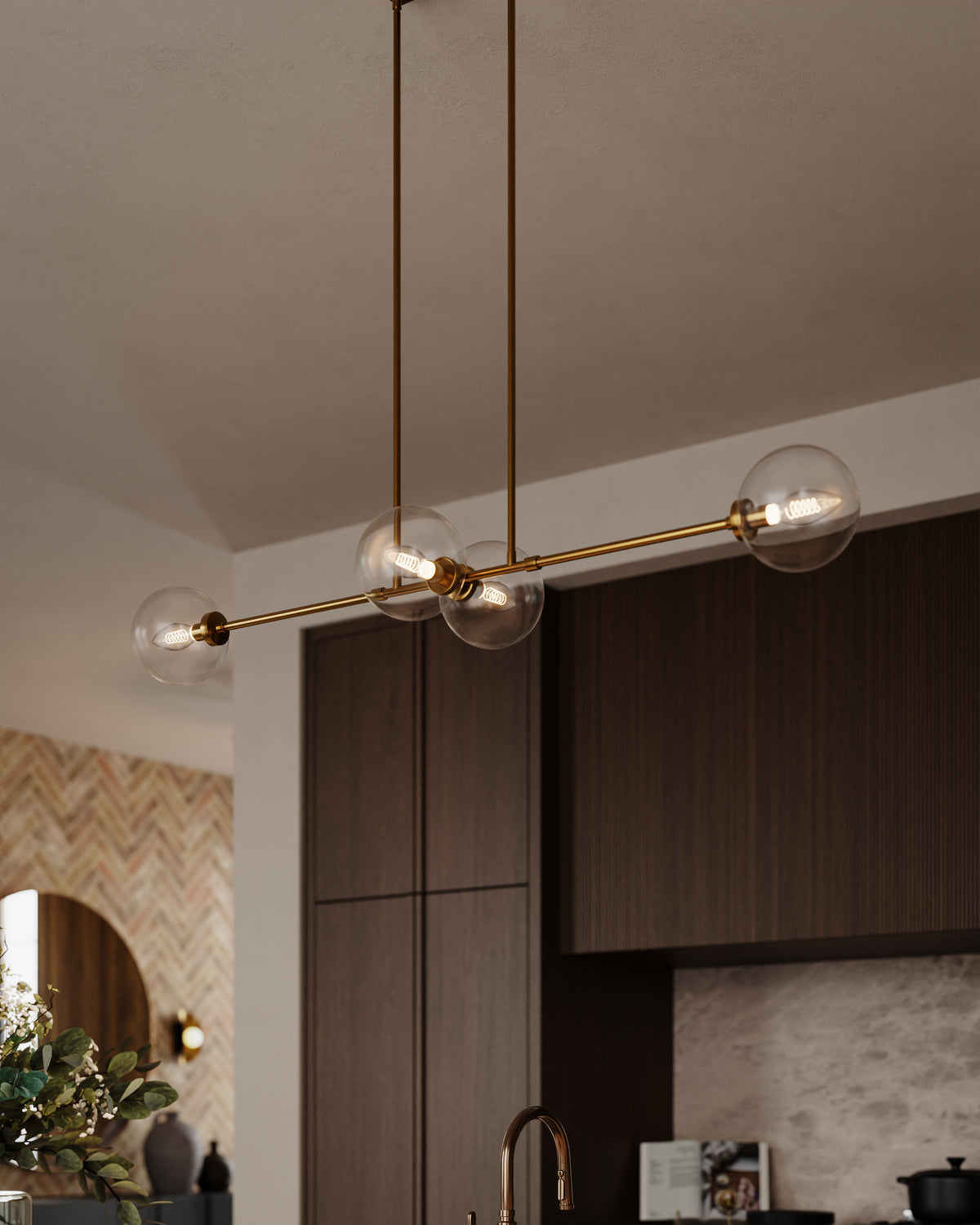 Modern linear pendant light with four clear glass globe shades on a brushed brass frame above a kitchen island.