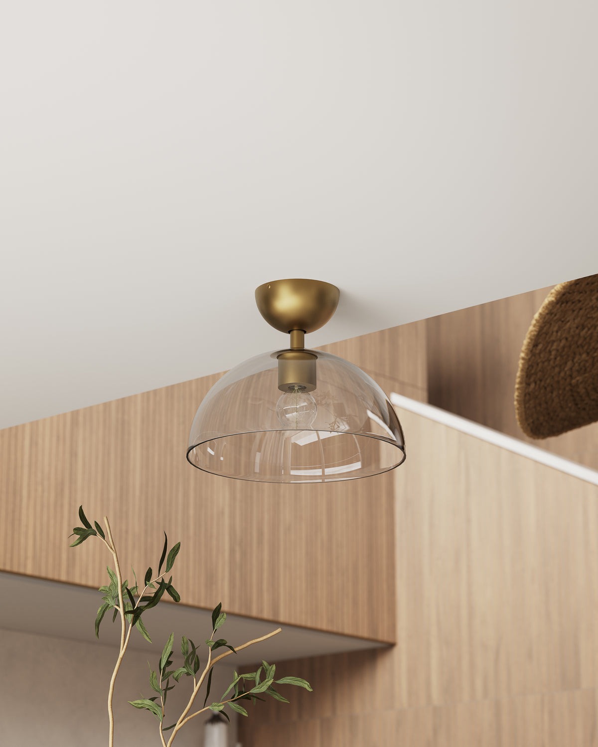 Semi flush mount ceiling light in brushed gold with a clear ribbed glass dome shade, placed above light wood cabinets and greenery to bring warm illumination to a modern kitchen.