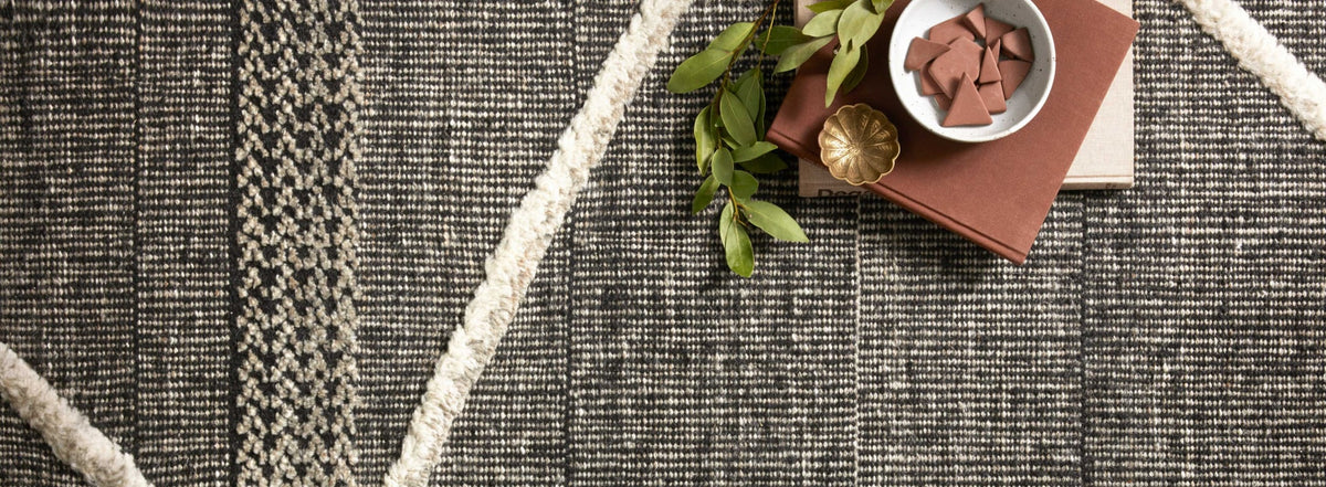 Hand knotted area rug in bold black and ivory tones with geometric patterns, styled with earthy decor for a modern yet timeless look.