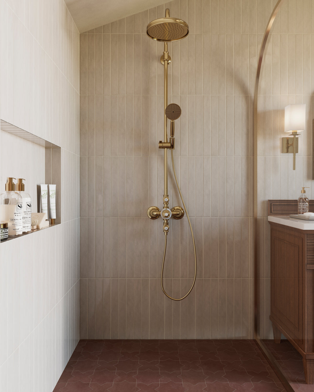 Walk-in shower with beige vertical wall tiles, brass rainfall showerhead, handheld shower fixture, recessed toiletry niche, and red patterned floor tile.