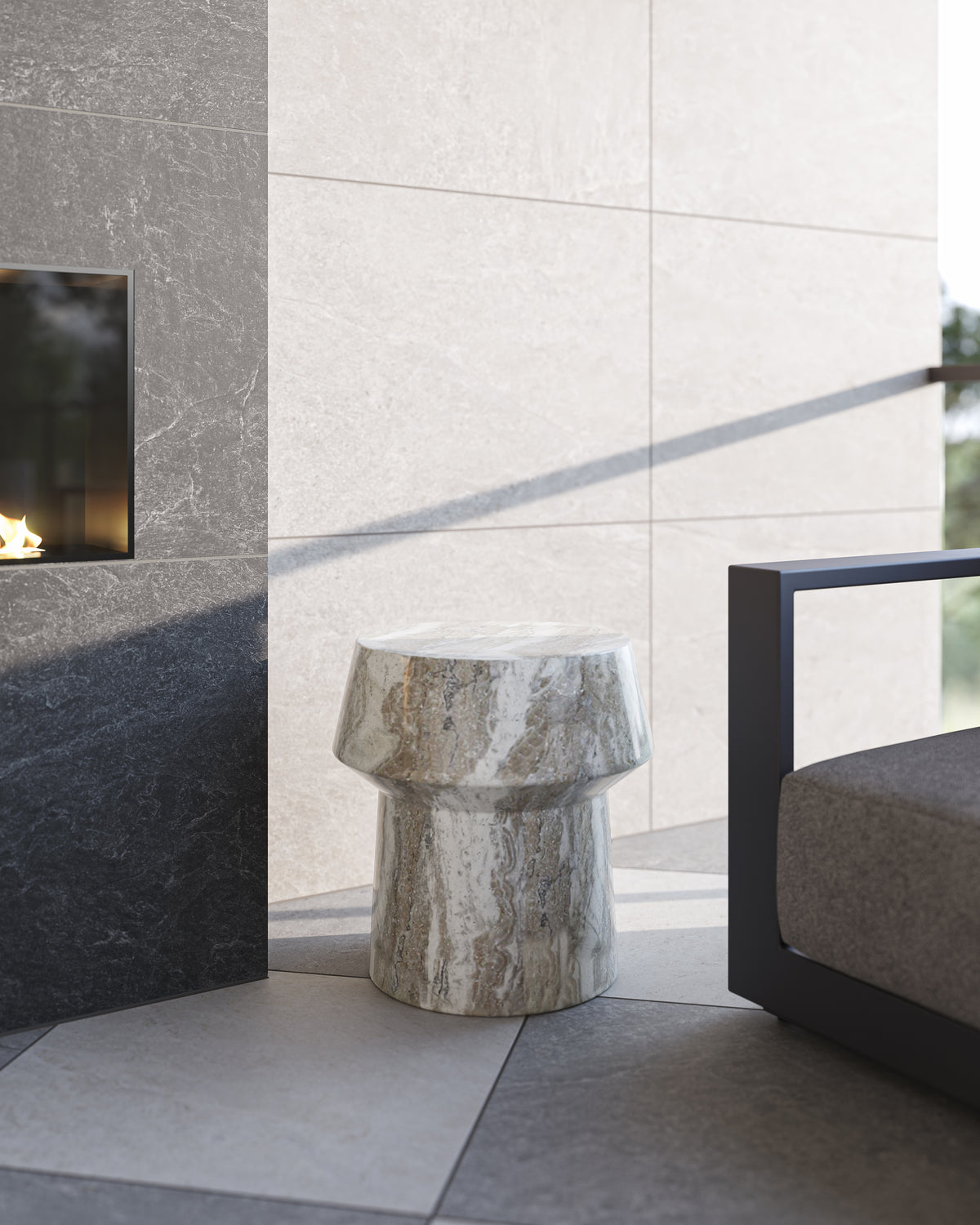 Beige and gray marble-like accent table with a polished stone finish placed beside a black metal lounge chair near a dark tiled fireplace and large cream wall tiles.