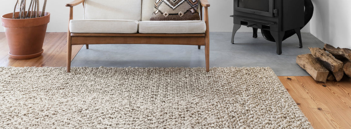 Cozy space featuring a chunky neutral-toned woven rug, complemented by a wooden bench, potted plant, and wood-burning stove.