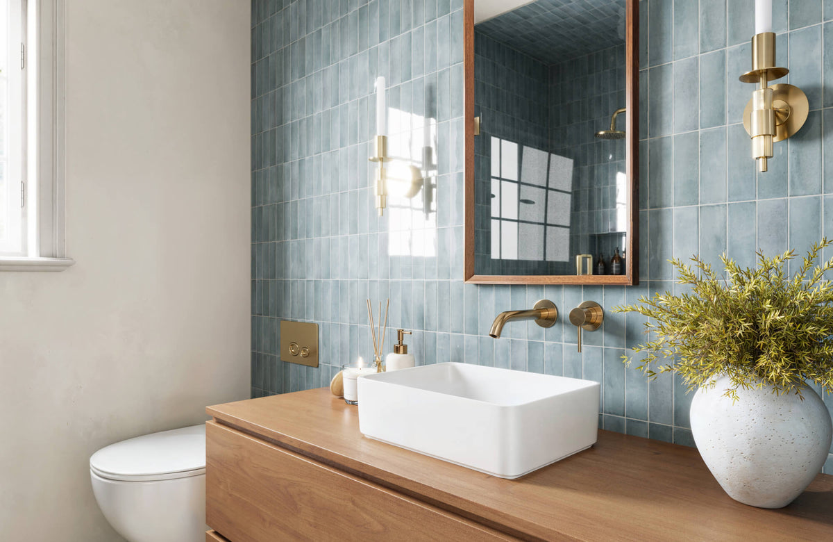 Blue vertical subway tile bathroom wall with brass fixtures, wood vanity, and square white vessel sink under framed mirror.