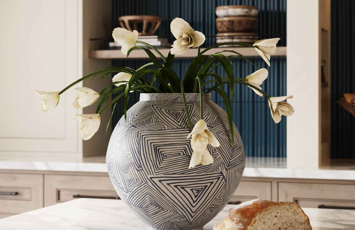 Large blue and white patterned ceramic vase filled with white flowers on a marble kitchen island, with open shelving and dark blue fluted tile in the background.