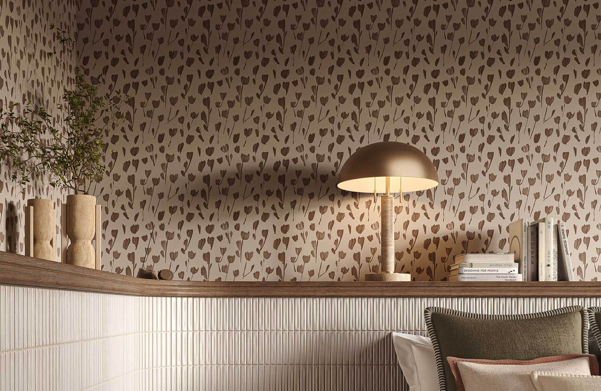 Contemporary interior with floral-patterned wallpaper, fluted cream subway tile wainscoting, a wood shelf, and a warm table lamp. 